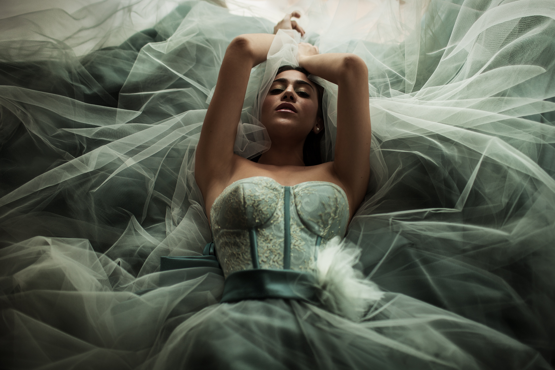 A model lying on a bed wearing a wedding dress. Looking rather ethereal.